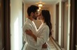 © Pete - Young couple wear white bathrobes embrace in hotel hallway near door. Lovers share tender moment before leaving room. Romance, intimacy, honeymoon vibes.
