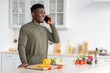 © Prostock-studio - Smiling Black Man In Casual Attire Talking With Smartphone While Preparing Healthy Salad Ingredients In Modern Kitchen. Engaged And Happy Young Adult Enjoying Cooking Session At Home.