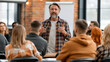 © pattozher - Workshop Facilitator Inspiring Audience: A charismatic middle-aged man with a beard passionately addresses a diverse group of attentive listeners in a workshop setting.
