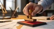 © Niju - A hand applying a rubber stamp to a document on a desk