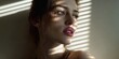 © Fun Factory - Close up portrait of a beautiful young woman with green eyes posing gracefully under soft window blinds light, sunlight casting sharp linear shadows across her smooth natural skin tone