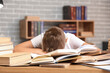© Pixel-Shot - Tired teenage boy with books at table in library