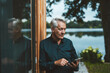 © Westend61 - Senior man with tablet PC standing by glass wall at backyard