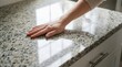© evgeniya - Hand touching clean polished granite kitchen countertop, close up, glossy surface, hygiene, modern home, cleanliness, day.