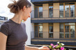 © Ina - Teenage girl enjoying warm sunlight on apartment balcony surrounded by blooming flowers. Peaceful summer lifestyle, wellbeing and mindful living concept in modern urban environment.