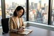 © TMGM - 高層ビルのオフィスでノートに書き込むベージュのジャケットを着た30代日本人女性