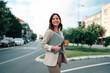 © Zamrznuti tonovi - Confident businesswoman holding laptop and coffee cup, walking outdoors on a city street, smiling
