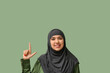 © Pixel-Shot - Beautiful young Muslim woman in hijab pointing at something on green background