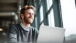 © aspac - Smiling man working on laptop near window in bright office space