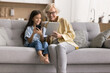 © fizkes - Multigenerational family using tablet and smartphone on pastime at home. Grandma and school-age granddaughter enjoy internet usage, learn new mobile application on weekend at home. Fun, tech, habit