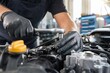 © Studio - Professional auto mechanic hands in black protective gloves repairing car engine with socket wrench in modern service garage, close-up view