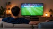 © Rhony - Young man watching soccer game on big television screen at home.