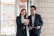 © amnaj - Young Asian business colleagues collaborating, smiling, and reviewing information on a digital tablet in a modern office environment