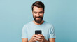 © Ace - Smiling young man using a smartphone against a blue background perfect for mobile communication digital technology and modern connectivity