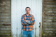 © Cavan Images - Serious man standing against a rustic barn wall