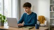 © OlgaNeuroArt - Smiling teenage boy working on a laptop at a desk in a home office. Young male student typing and studying online with a notebook. Remote learning and youth entrepreneurship concept