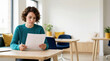 © OlgaNeuroArt - Young businesswoman reading document at desk in modern office. Focused female professional reviewing contract paperwork