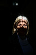 © Connect Images - Woman with blonde hair stands in dramatic lighting, casting shadows on her face.