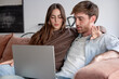 © luciano - Couple relaxing on a sofa watching content on a laptop at home, communicating and sharing screens