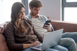 © luciano - Couple relaxing at home, connected to technology, browsing and multitasking on laptop and smartphone