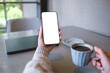 © Farknot Architect - Mockup image of a woman holding mobile phone with blank desktop screen and drinking coffee with laptop on the table