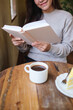 © Farknot Architect - Vertical closeup image of a woman reading a book with coffee cup and a lemon cake on the table
