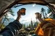© wasis - Inside view of a tent, arms holding mugs in a toast against a bright sunlit mountain vista