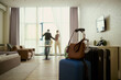© DragonImages - Wide angle view of young couple arriving in hotel room, unpacking luggage and starting vacation stay, checking view from window. Travel booking, hospitality marketing, family tourism promotion