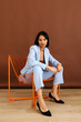 © Tania Cervian/Stocksy - Woman in light blue suit sitting on orange chair