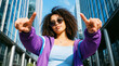 © jack - Confident young woman pointing at camera in urban cityscape wearing sunglasses and purple jacket