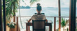 © Jana - Woman sitting at a desk on a balcony working on a laptop with an ocean view