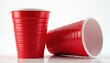 © Maryna - Two red plastic cups with white rims rest on a white surface. One cup stands upright, the other lies on its side. These disposable containers are often used for parties.