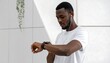 © Muhammad - A dark-skinned man wearing white shirt and earbuds looks at watch