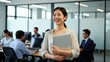 © Ganesha88 - Cheerful professional woman with laptop in contemporary office environment while coworkers focus on their tasks in the background