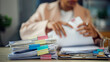 © WARAPHON - Woman reviews papers at cluttered desk. Fingers trace document edges. Stacks of folders rise beside her. Colorful clips hold each file. Focused, she organizes daily tasks. Ideal for business, finance