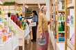 © pressmaster - Caucasian middle aged woman browsing cosmetic products in beauty store, comparing skincare options and retail choices. Useful for beauty retail, consumer shopping, family purchase