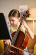 © DragonImages - Vertical shot of Caucasian girl studying music and playing cello while reading sheet notes, showing focused arts education and skill development. Ideal for music school promotion