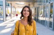 © Ajay - Smiling woman in a yellow patterned dress stands outdoors near modern glass buildings