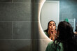 © Marko Geber - Woman examining face in home bathroom mirror
