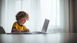 © Lady O - A boy is sitting at the table and doing homework with his laptop, drawing on paper, concept of homeschooling.