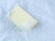 © Eka - Kitchen sponge floating in rich white soap foam and bubbles. Close-up background of cleaning process with detergent, shampoo, or soap suds, representing hygiene, housework, and sanitizing