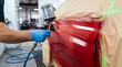© Kate Mayer - Worker spray painting a red car in an auto body shop. Vehicle restoration, professional craftsmanship, automotive repair, manufacturing process.