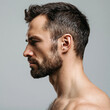 © Olga Ко - > Side profile portrait of a handsome Caucasian man with a beard and bare shoulders. Men's grooming, skincare, and barbershop concept on gray background.