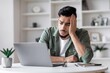 © Prostock-studio - Worried Young Hispanic Man Sitting At Home Office While Working On Laptop, Showing Signs Of Stress And Frustration. Setting Shows Modern Office Space With Minimalistic Interior Design.
