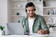 © Prostock-studio - Smiling Middle Eastern Man Wearing Headset And Taking Notes While Working On Laptop From Home Office. Focused On Task And Engaged In Work At Modern Workspace. Business Concept.