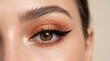 © photoplotnikov - Close up of single female eye with shimmery copper eyeshadow and bold winged eyeliner, highlighted inner corner and long lashes showcasing makeup detail and skin texture