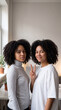© Professor - Two happy young black women standing close together and smiling warmly while one makes a peace sign gesture near a window