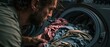 © COK House - A bearded man intently examines colorful laundry inside a washing machine, serving as a domestic background for themes of household chores and daily routine.