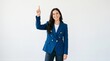 © MUNAWAR - Woman in blue blazer pointing upwards with a smile on her face indoors.