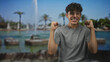 © Krakenimages.com - Boy clenches fists and smiles with eyes shut in front of a fountain and palm trees at a public park; triumph joy youthful energy.